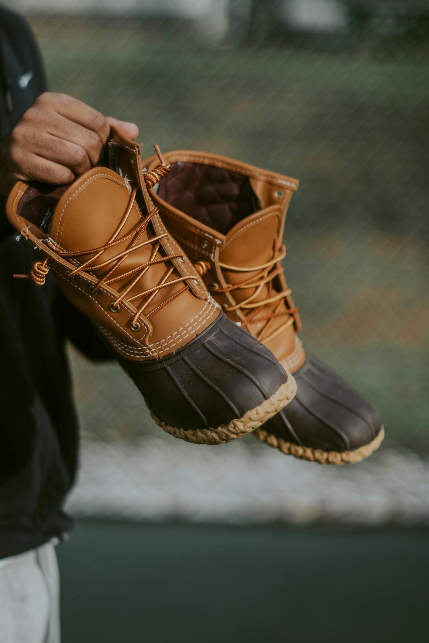 Close-up of a pair of brown leather and rubber ankle boots being held outdoors.