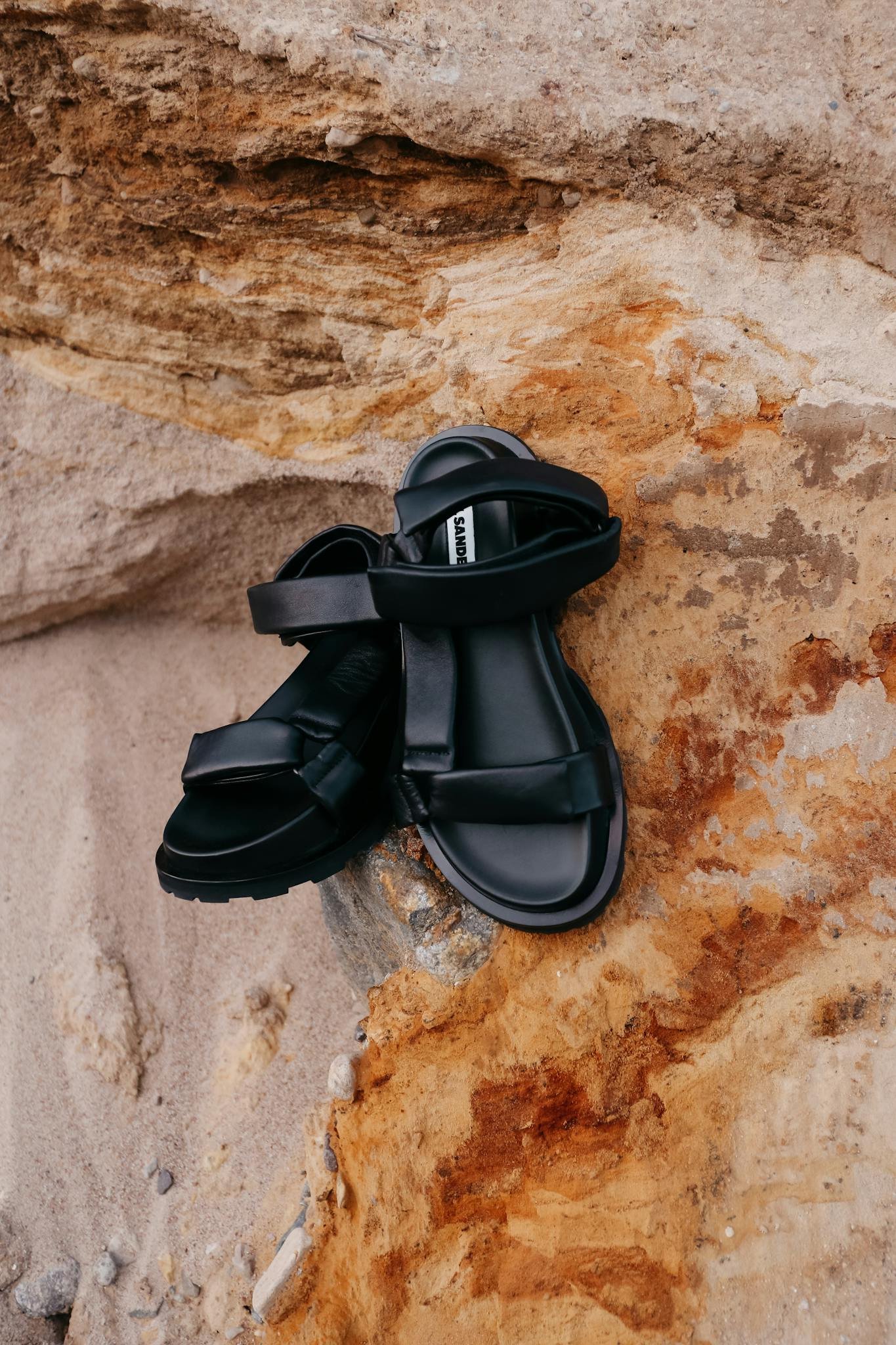 Close-up of black sandals placed on textured rock and sand surface.