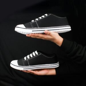 Pair of black sneakers held in hands against a dark background, showcasing minimalist fashion footwear.