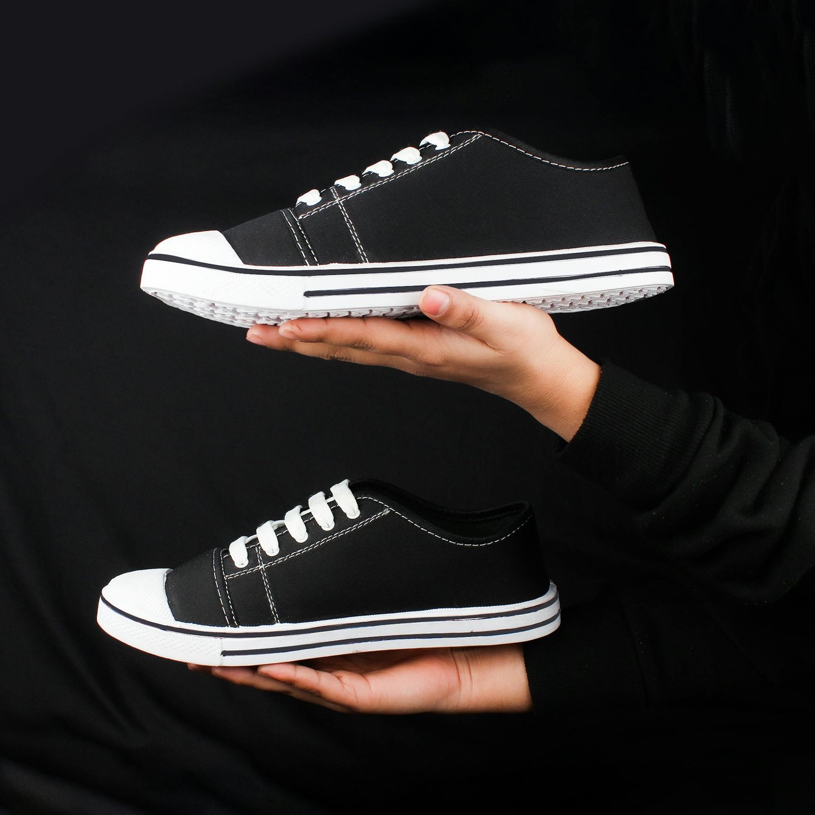 Pair of black sneakers held in hands against a dark background, showcasing minimalist fashion footwear.